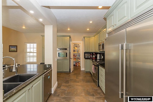 kitchen with appliances with stainless steel finishes, dark stone countertops, dark tile flooring, and sink