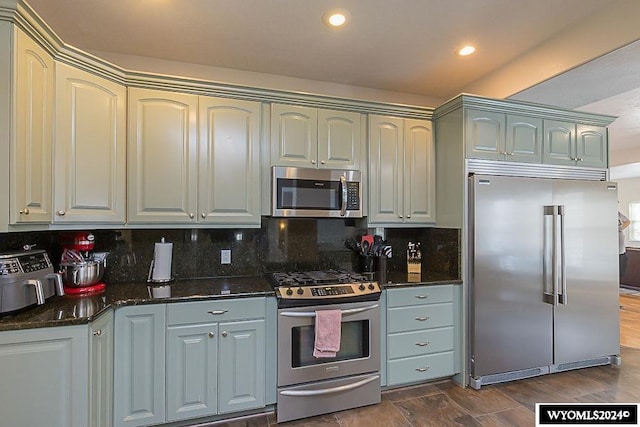 kitchen featuring appliances with stainless steel finishes, dark hardwood / wood-style floors, tasteful backsplash, and dark stone countertops