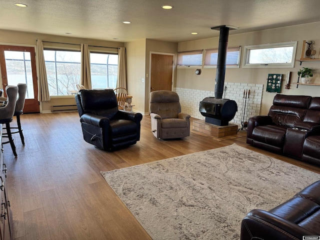 living room featuring a baseboard heating unit, a textured ceiling, a wood stove, and hardwood / wood-style floors