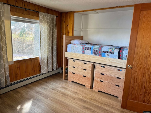 bedroom with wood walls, baseboard heating, light hardwood / wood-style flooring, and a textured ceiling