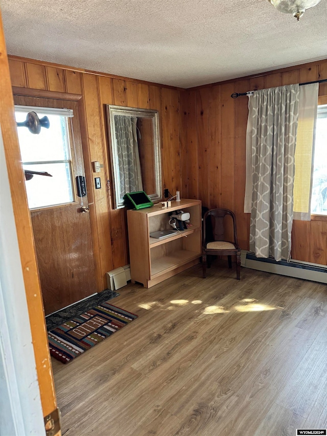 foyer entrance featuring a baseboard heating unit, wooden walls, wood-type flooring, and a textured ceiling