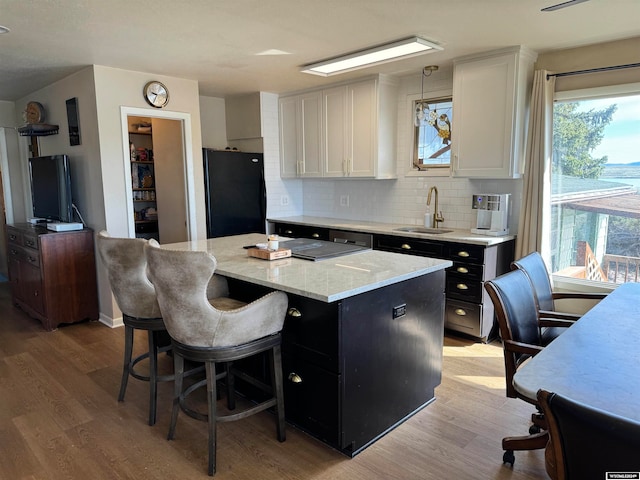 kitchen with light wood-type flooring, black fridge, backsplash, sink, and white cabinets