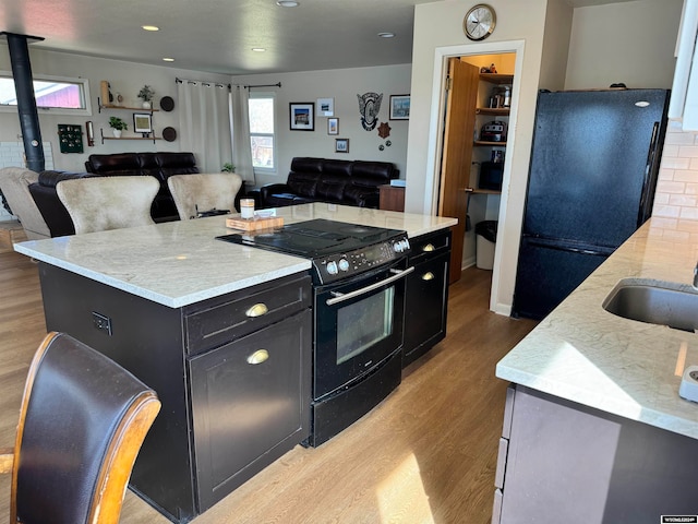 kitchen featuring a center island, light hardwood / wood-style flooring, black appliances, light stone counters, and sink