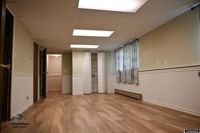 interior space featuring a drop ceiling, a baseboard heating unit, and light hardwood / wood-style floors