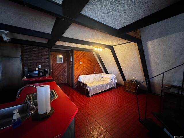 carpeted bedroom featuring brick wall, wooden walls, beam ceiling, and a textured ceiling