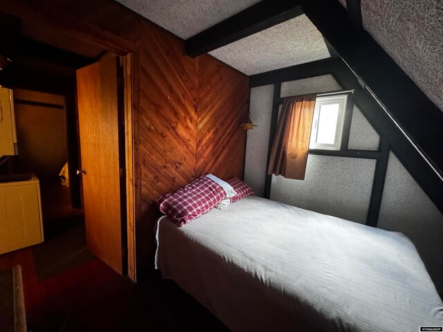 bedroom featuring beamed ceiling, a textured ceiling, and wood walls