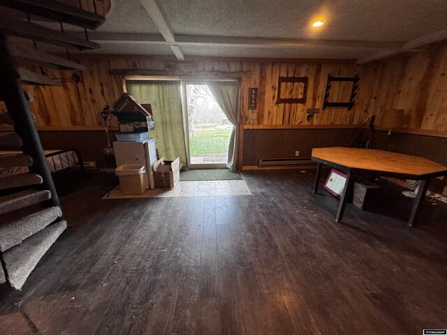 dining area featuring a baseboard heating unit, a textured ceiling, wood walls, and dark wood-type flooring