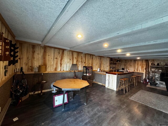 rec room with beam ceiling, a textured ceiling, dark wood-type flooring, and wood walls