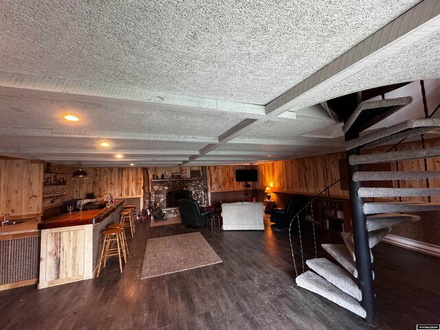 interior space featuring wooden walls, dark hardwood / wood-style flooring, a textured ceiling, and a stone fireplace