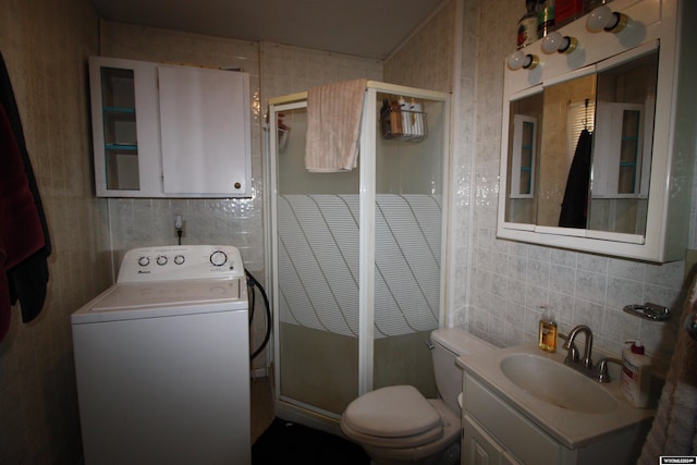 bathroom featuring washer / dryer, toilet, a shower with door, vanity, and tile walls