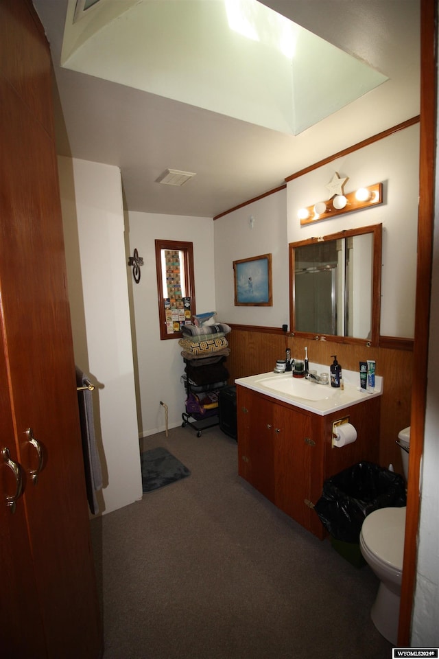 bathroom with vanity, wooden walls, a skylight, toilet, and a shower with shower door