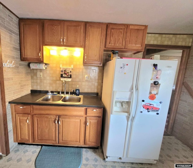 kitchen featuring brick wall, white fridge with ice dispenser, and sink