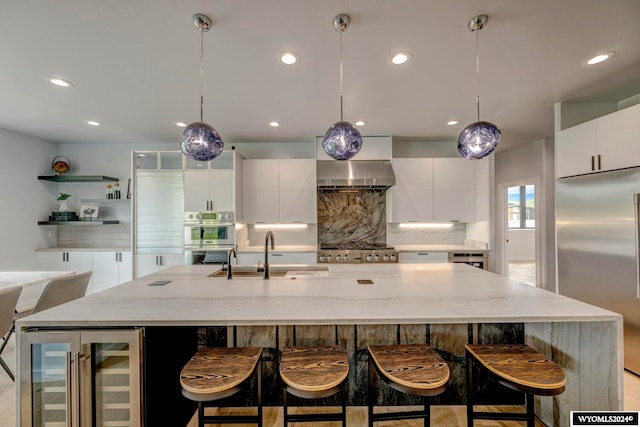 kitchen featuring wall chimney range hood, a center island with sink, stainless steel appliances, beverage cooler, and backsplash