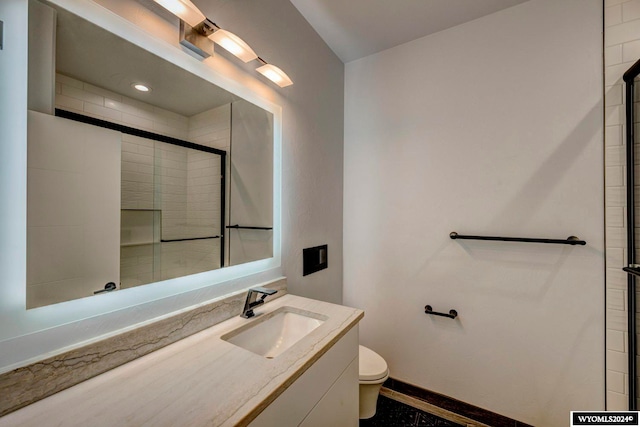 bathroom featuring a shower with shower door, toilet, and vanity with extensive cabinet space