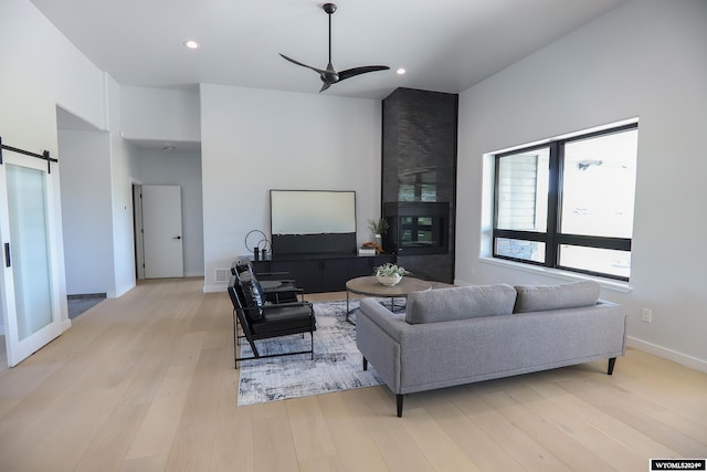 living room with a barn door, ceiling fan, light hardwood / wood-style flooring, and a large fireplace