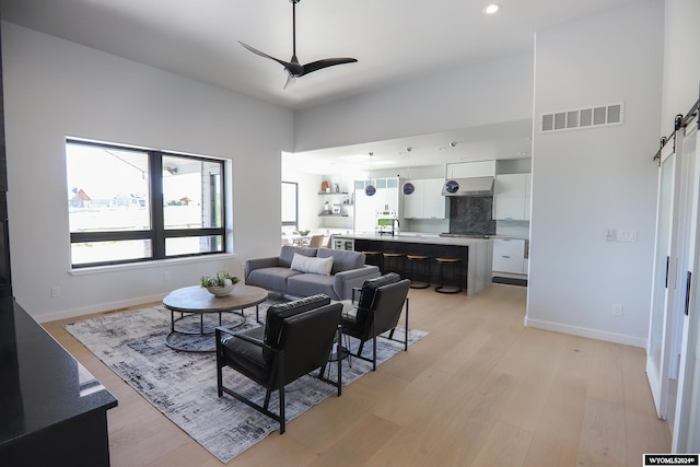 living room featuring a barn door, sink, ceiling fan, and light hardwood / wood-style flooring