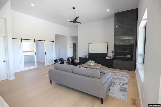 living room with a barn door, light hardwood / wood-style floors, a fireplace, and ceiling fan