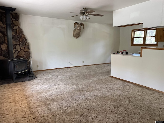 unfurnished living room featuring carpet flooring, ceiling fan, and a wood stove