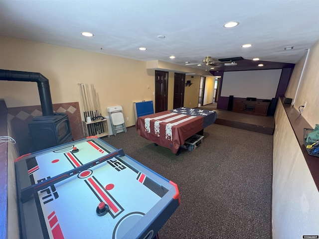 recreation room featuring carpet flooring, a wood stove, and ceiling fan