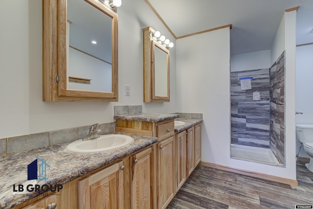 bathroom featuring crown molding, hardwood / wood-style floors, vanity, a tile shower, and toilet