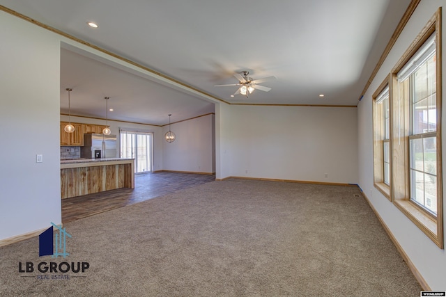 unfurnished living room with crown molding, ceiling fan with notable chandelier, and dark colored carpet