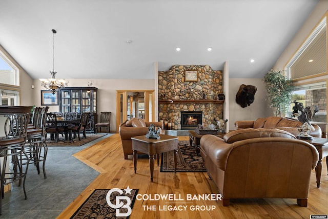 living room with a notable chandelier, a stone fireplace, hardwood / wood-style floors, and lofted ceiling