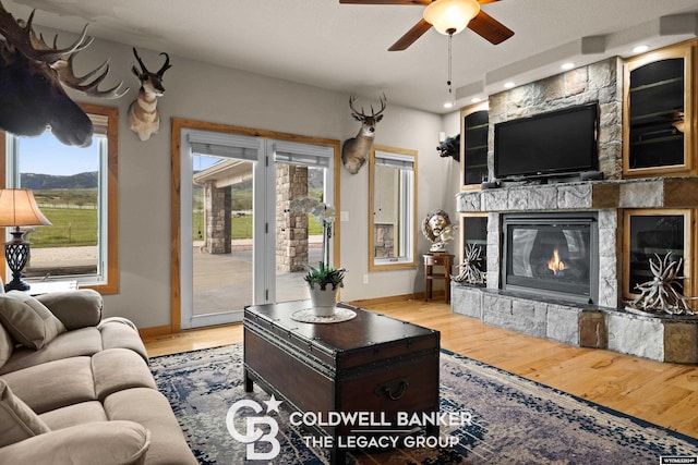 living room featuring ceiling fan, light wood-type flooring, and a fireplace