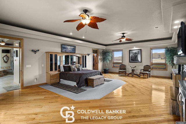 bedroom featuring ensuite bathroom, a raised ceiling, ceiling fan, and light wood-type flooring