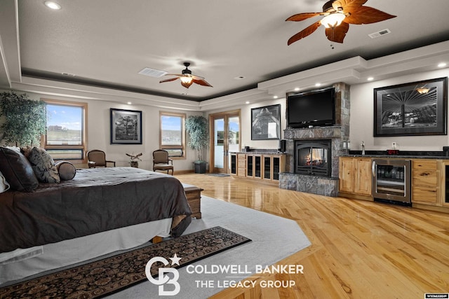 bedroom featuring access to exterior, a multi sided fireplace, wine cooler, a tray ceiling, and light wood-type flooring