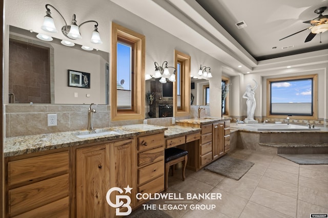 bathroom with tile patterned flooring, vanity, tiled bath, and ceiling fan