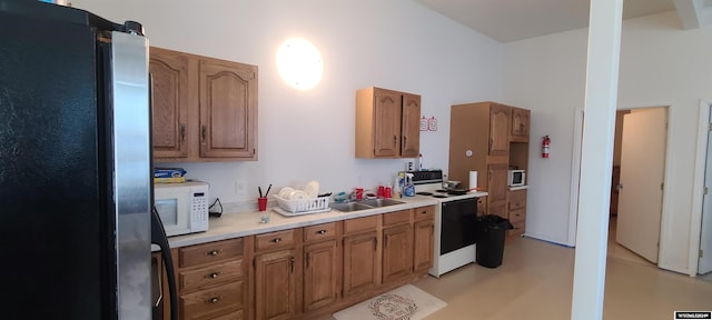 kitchen featuring range with electric cooktop, white microwave, freestanding refrigerator, light countertops, and a sink