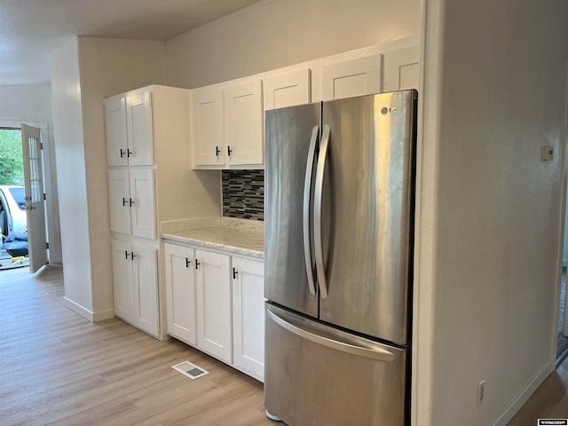 kitchen featuring light stone counters, white cabinetry, light hardwood / wood-style flooring, backsplash, and stainless steel fridge