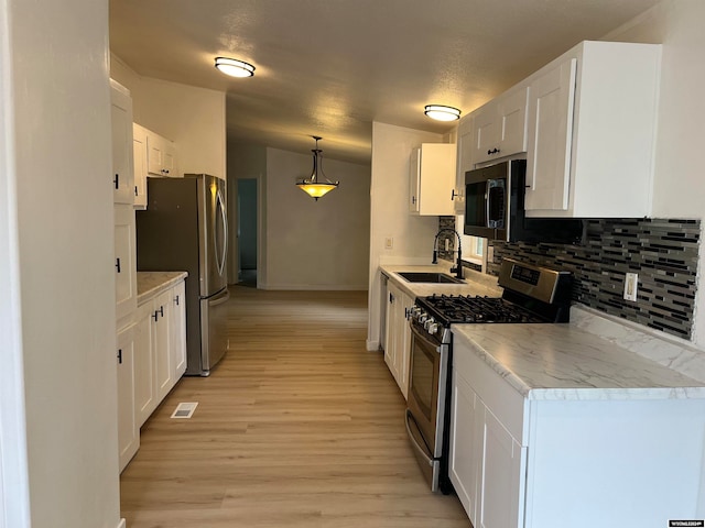 kitchen with hanging light fixtures, vaulted ceiling, white cabinets, stainless steel appliances, and sink