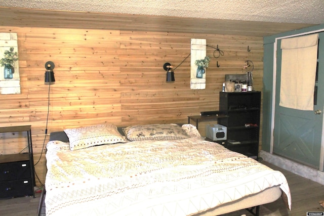 bedroom featuring a textured ceiling, dark hardwood / wood-style floors, and wood walls