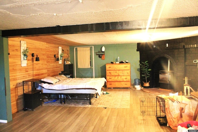 bedroom with wood-type flooring, wood walls, beam ceiling, and a textured ceiling