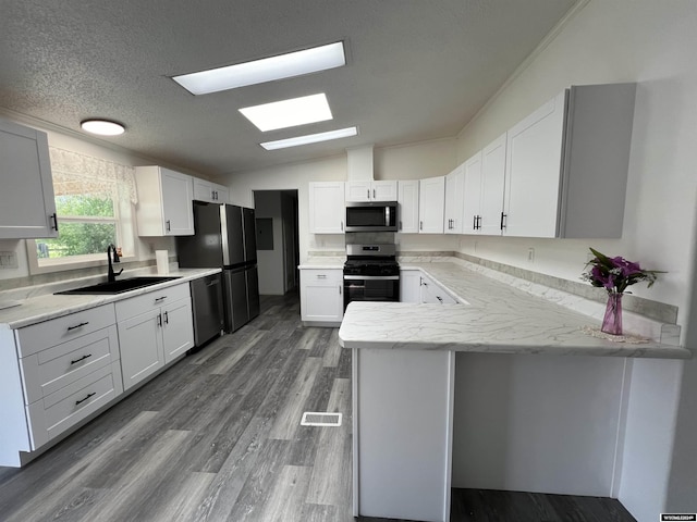 kitchen featuring kitchen peninsula, appliances with stainless steel finishes, lofted ceiling with skylight, sink, and white cabinets