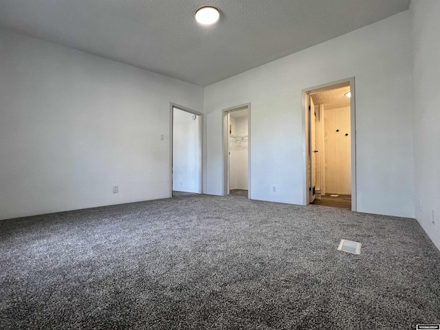 unfurnished bedroom with carpet flooring, connected bathroom, a spacious closet, a textured ceiling, and a closet