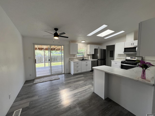 kitchen with kitchen peninsula, vaulted ceiling with skylight, dark hardwood / wood-style floors, white cabinetry, and stainless steel appliances