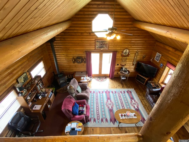 living room with hardwood / wood-style flooring, a wood stove, rustic walls, wood ceiling, and ceiling fan