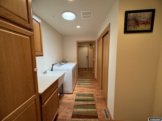 laundry room featuring washer and clothes dryer, cabinets, light wood-type flooring, and sink