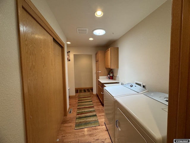 washroom with cabinets, washing machine and dryer, and light wood-type flooring