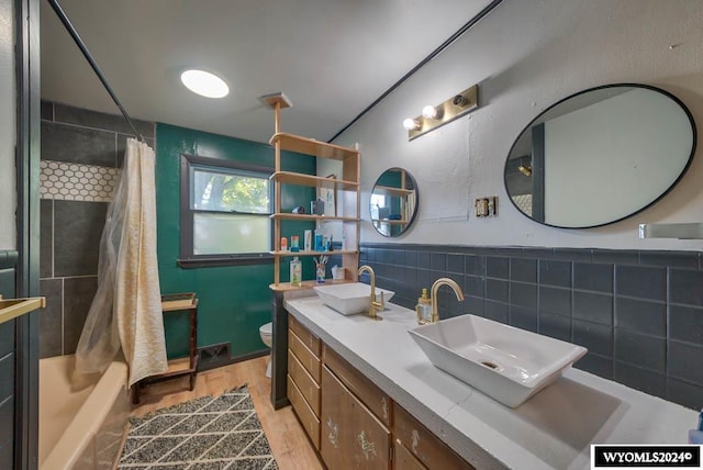 full bathroom featuring hardwood / wood-style floors, toilet, shower / bath combo with shower curtain, vanity, and tile walls