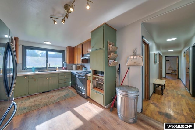 kitchen with appliances with stainless steel finishes, light hardwood / wood-style flooring, green cabinetry, and sink