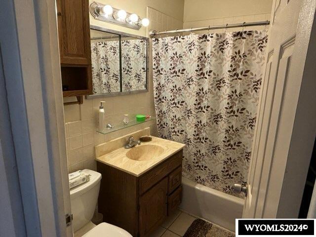 full bathroom with shower / bath combination with curtain, vanity, tile walls, tile patterned flooring, and toilet