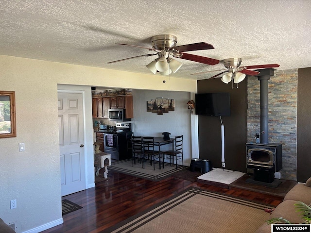 living room with dark hardwood / wood-style floors, ceiling fan, a wood stove, and a textured ceiling