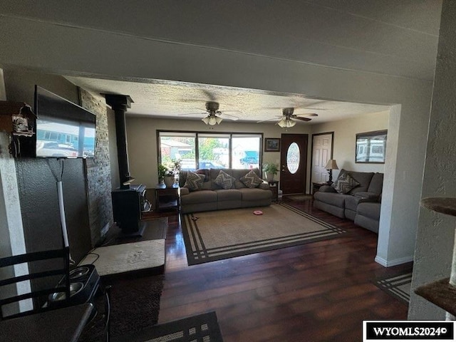 living room featuring ceiling fan, dark hardwood / wood-style flooring, a wood stove, and a textured ceiling