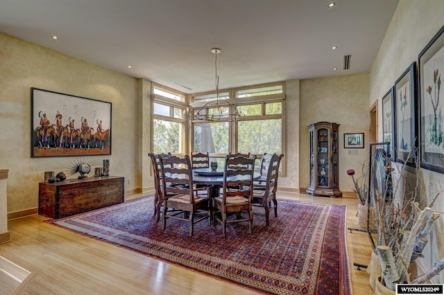 dining space featuring a notable chandelier, a towering ceiling, and light wood-type flooring