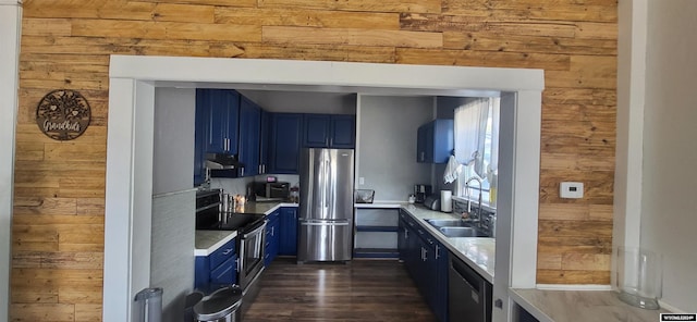 kitchen with appliances with stainless steel finishes, sink, blue cabinetry, and wooden walls