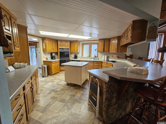 kitchen featuring a drop ceiling, a center island, a breakfast bar area, double oven, and light tile patterned floors