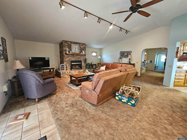 living room featuring rail lighting, ceiling fan, light colored carpet, a fireplace, and vaulted ceiling